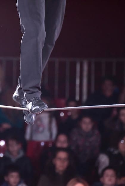 A conceptual image representing a tightrope walker balancing precariously between two separate movie theater screens, one displaying a horror film scene and the other showing a romantic comedy scene. The image visually captures the challenge of balancing different genre elements to create a successful genre-bending film.