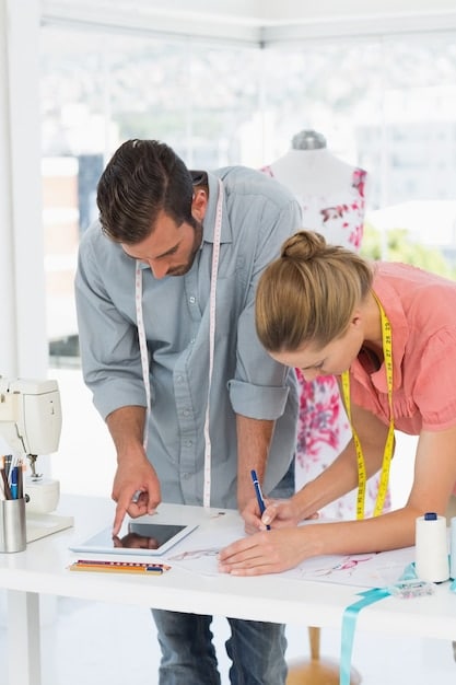 A wide shot of a seamstress and a designer discussing costume design together, while the designer is sketching out some ideas in a notebook.