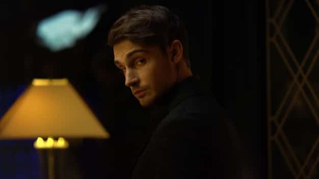 Close-up shot of Kendall Roy, looking stressed and determined. He is wearing a tailored suit and standing in a dimly lit room. The background is blurred, emphasizing his isolation and intensity.
