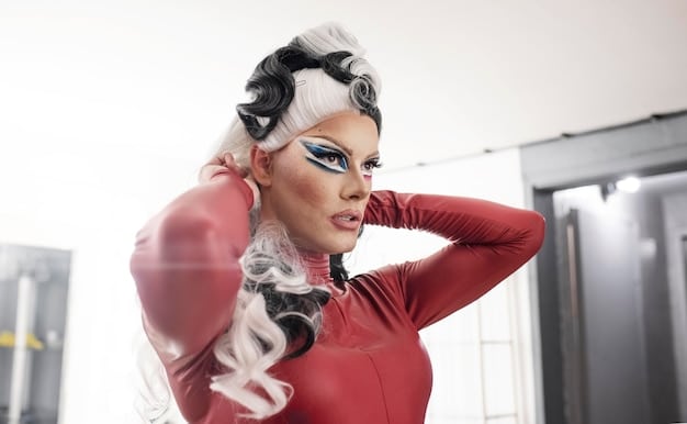 RuPaul in full drag, judging a contestant on RuPaul's Drag Race, with a brightly lit stage as the backdrop.