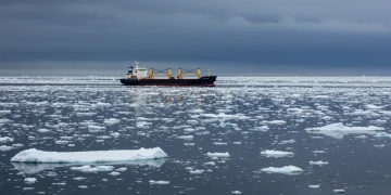 Cargo ship navigating through melting Arctic ice, symbolizing increased shipping and environmental challenges.