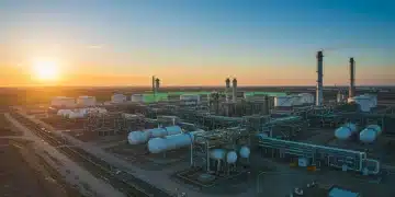 Industrial natural gas facility with pipelines and storage tanks under a green-tinted sky, symbolizing methane reduction efforts.