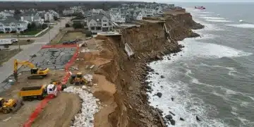 Severely eroded U.S. coastline in 2026, with damaged homes and emergency barriers.